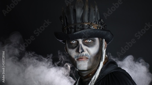 Sinister man with Halloween skeleton makeup turning his head and looking at camera, trying to scare