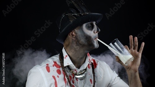 Scary guy in carnival costume of Halloween skeleton looking at camera  drinks milk from a glass