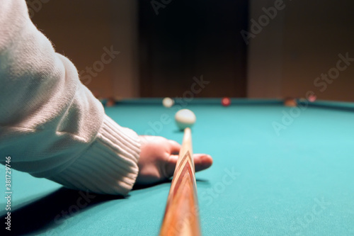 Hand with cue aiming on billiard ball at table. Process game.