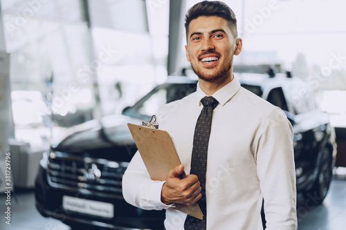 Tableau sur toile Friendly handsome car seller man standing in car salon