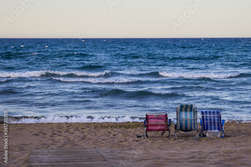 Tres sillas en la orilla del mar mirando el horizonte del océano y playa con orilla de arena y olas pequeñas