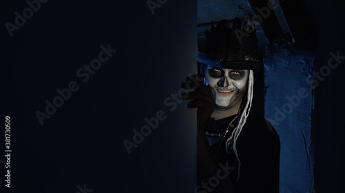 Creepy man with Halloween skeleton makeup slowly appears from dark corner with frightening smile © Andrii Iemelianenko