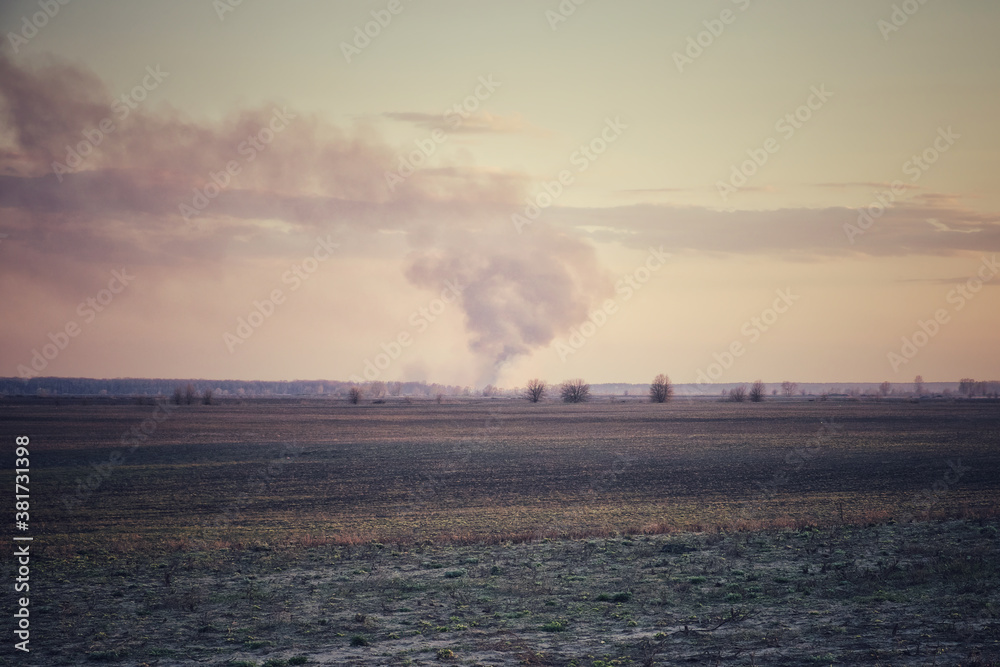 Smoke from a large fire over an agricultural field in the evening. Puffs of smoke in the sunset sky.