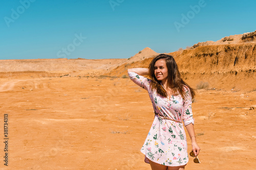 A young woman with long hair in a short dress walks through the orange rocky desert on a hot day