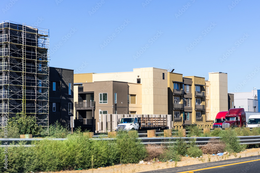 Modern apartment buildings new and under construction in Silicon Valley; heavy trucks driving on the freeway, right next to the residential buildings; East San Francisco bay area, California