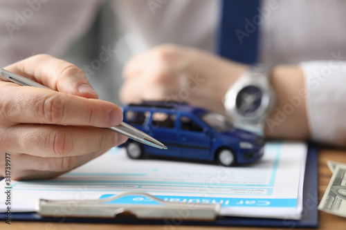 Male hands hold ballpoint pen over car insurance blank and toy car. Car insurance concept.