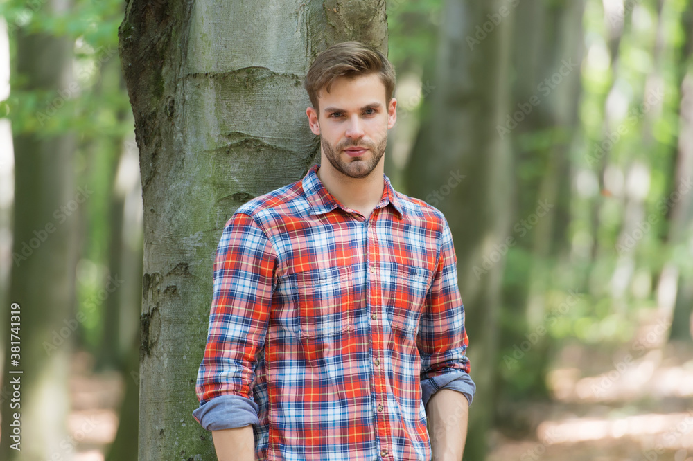 perfect hair. casual fashion style. muscular man in forest. sexy macho in unbuttoned shirt outdoor. young unshaven man has groomed hair. male beauty and fashion. guy with bristle wear checkered shirt