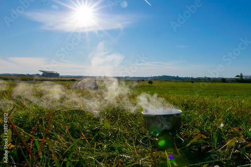 Camping stove and steam coming out of the bowl in a sunny spring day with blue sky during camping adventure. Lithuania countryside. photo