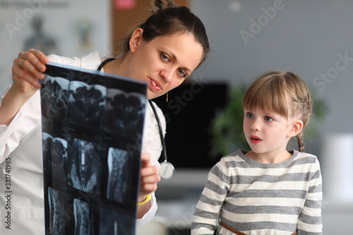 Woman doctor shows child patient an xray in clinic. Use of radiation diagnostics of diseases of skeletal system in pediatric practice concept.