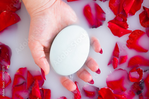 Female hand hold soap against the background of milk or white water with rose petals