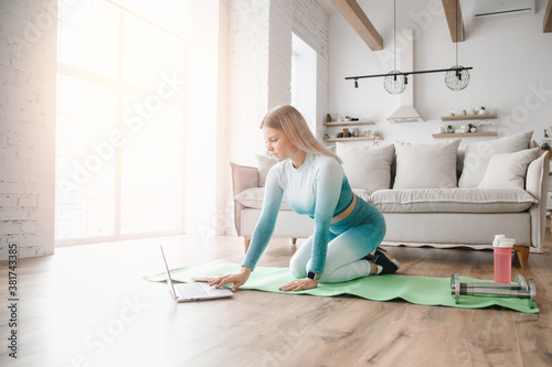 Slim sporty woman in sportswear in living room and is using laptop at home. Concept online sport workout and trainer yoga