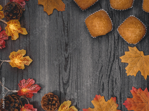  muffins and autumn leavesmuffins, fall leaves, pine cones and garland on a black wooden table with a place for text in the middle, top view close-up.