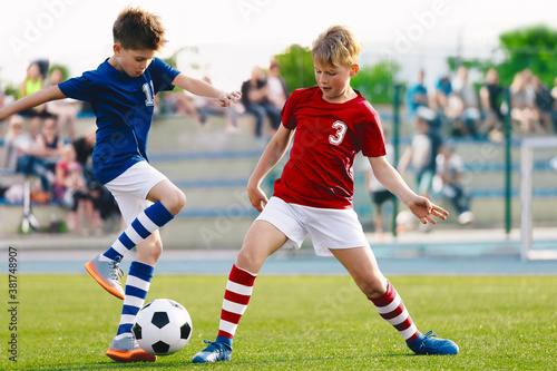Happy kids compete in football game. Running soccer players. Competition between players running and kicking football ball. Football school. Young boys playing soccer game. Kids having fun in sport. © matimix