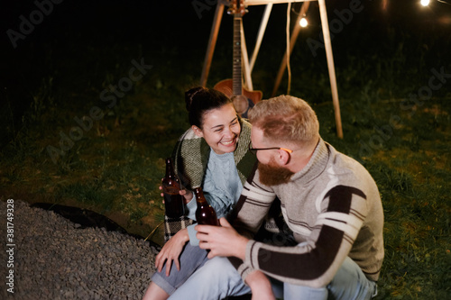 Couple have a good time together on night picnic drinking beverage from bottles