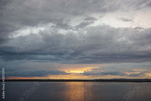 Dramatic cloudscape at sunset. Reflection of the sky in the water. Thunderclouds over the lake. © Natalia