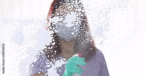 One young woman cleaning home, wiping and doing disinfection on windows, Young Woman with a face mask cleaning window at home
