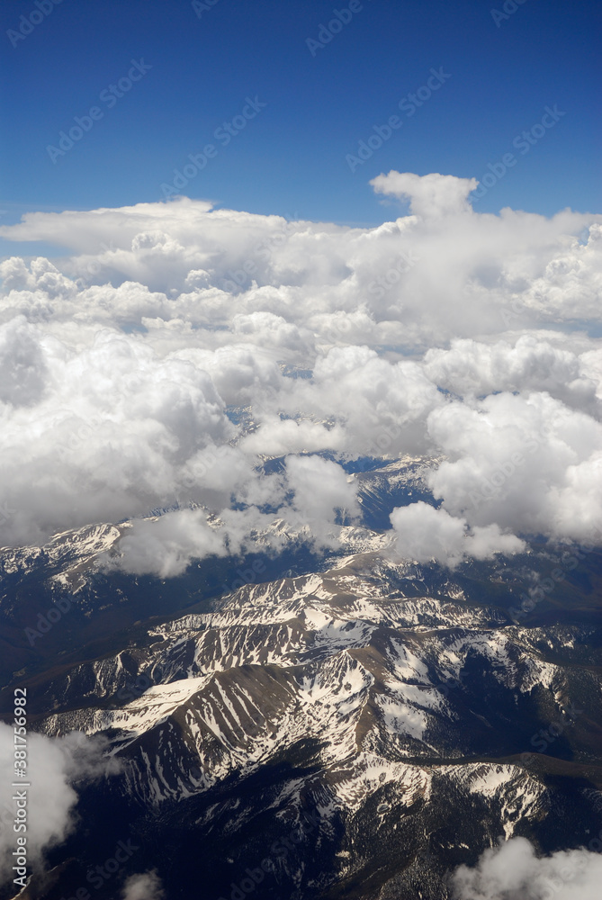 Aerial photo of Rocky Mountains with puffy white clouds and blue sky