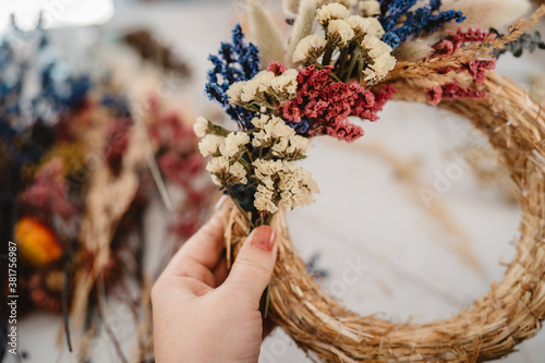 Fototapeta Naklejka Na Ścianę i Meble -  Girl making floral door wreath from colorful dry summer flowers and plants.  Fall flower decoration workshop