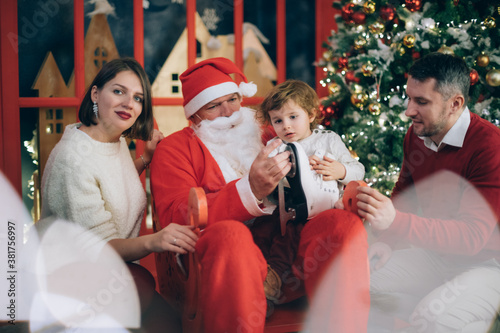 Family with a child and Santa Claus near a New Year tree in Christmas decorations.