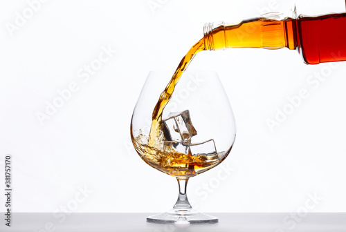 Pouring whiskey drink into glass with ice cubes on white background