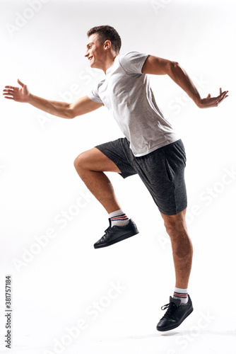 athlete man in sneakers shorts and a t-shirt on a light background and running to the side in full growth
