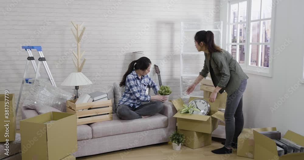 slow motion of asian young girls unpacking cardboard boxes at new home in cozy bright living room. two lady roommates moving house together living best friendship. women discussing home interior. slow motion of asian young girls unpacking cardboard boxes at new home in cozy bright living room. two lady roommates moving house together living best friendship. women discussing home interior.