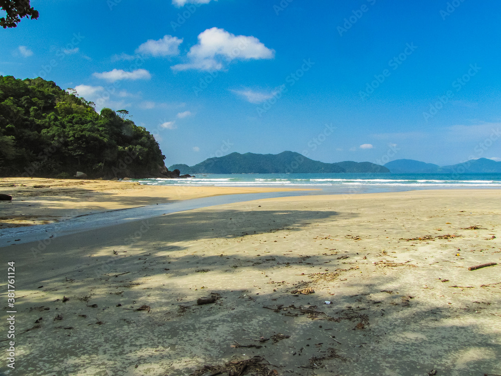 Praia Brava da Fortaleza in Ubatuba/SP, Brazil, on a sunny day. A small stream flows across the sandy beach into the ocean, surrounded by preserved nature and turquoise waters Praia Brava da Fortaleza in Ubatuba/SP, Brazil, on a sunny day. A small stream flows across the sandy beach into the ocean, surrounded by preserved nature and turquoise waters