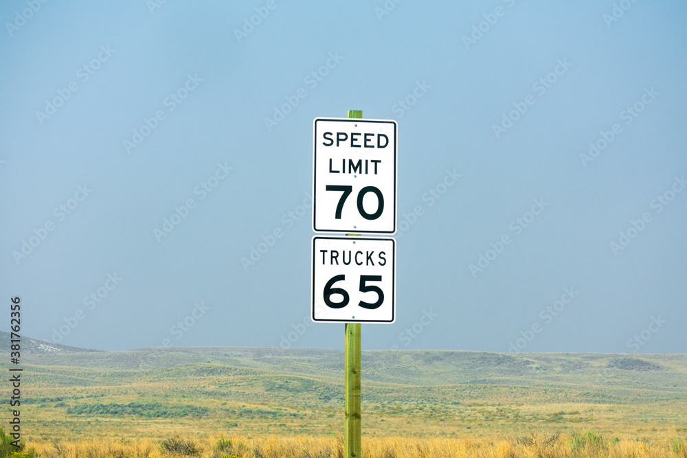 Seventy mph speed limit, Trucks 65 sign on wooden post. Speed zone traffic sign against desert landscape. Seventy mph speed limit, Trucks 65 sign on wooden post. Speed zone traffic sign against desert landscape.