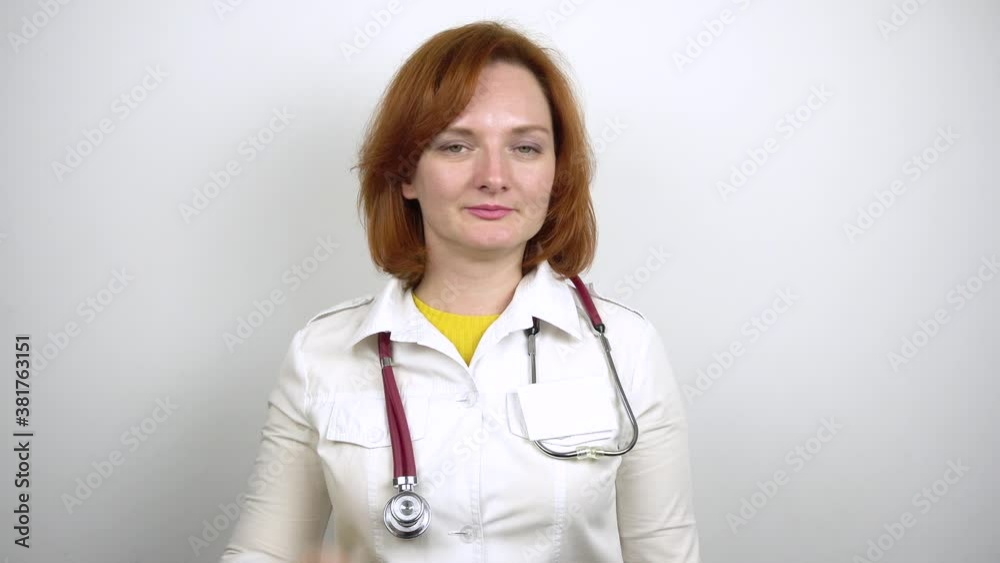 Young woman in white medical gown shows thumbs up attention.Doctor with a stethoscope around his neck.White background.4k Young woman in white medical gown shows thumbs up attention.Doctor with a stethoscope around his neck.White background.4k