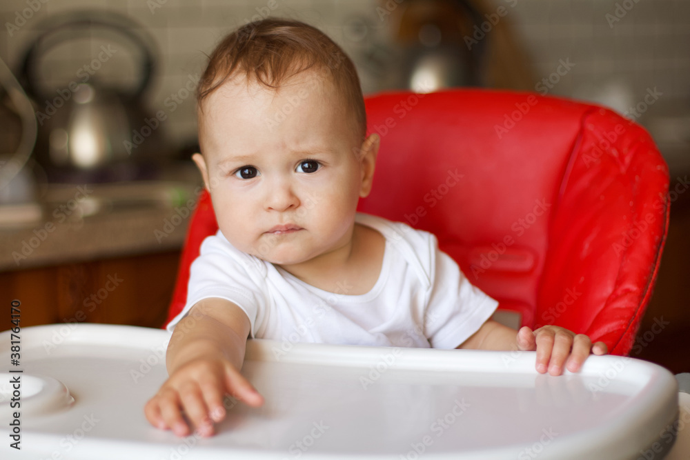 Adorable cute baby boy with a serious look sits in the highchair, close-up portrait.