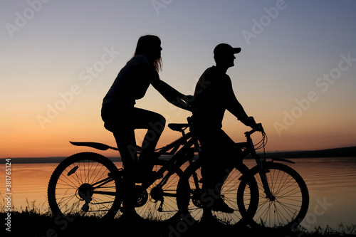 silhouette of friends on bicycle.sunset sky.  couple cyclist go along coast.
