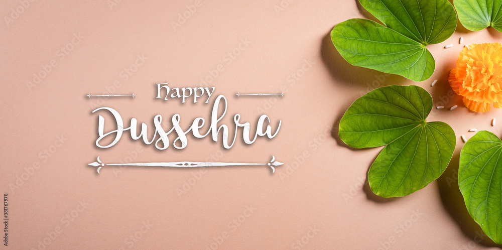 Happy Dussehra. Yellow flowers, green leaf and rice on orange pastel background. Dussehra Indian Festival concept.