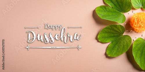 Happy Dussehra. Yellow flowers, green leaf and rice on orange pastel background. Dussehra Indian Festival concept.