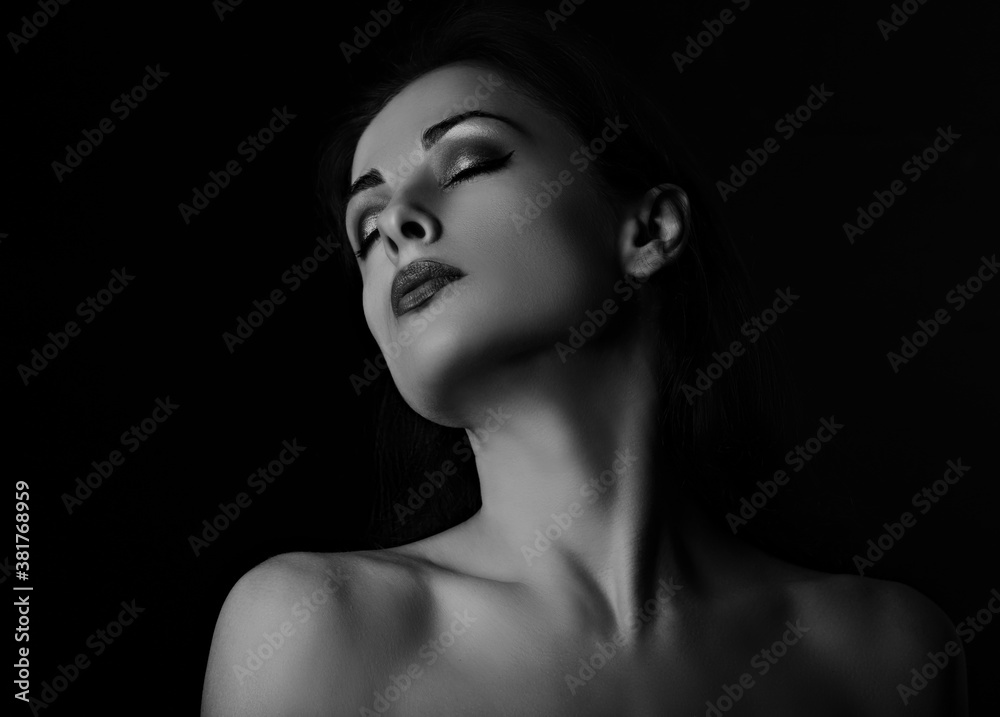 Beautiful mysterious smokey eyes makeup woman in darkness posing with healthy tan yellow skin tone elegant strong neck on black background with empty copy space. Closeup portrait.
