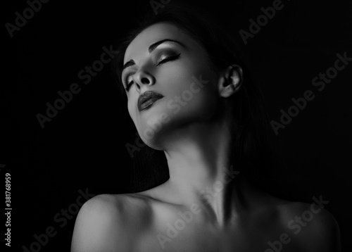 Beautiful mysterious smokey eyes makeup woman in darkness posing with healthy tan yellow skin tone elegant strong neck on black background with empty copy space. Closeup portrait.