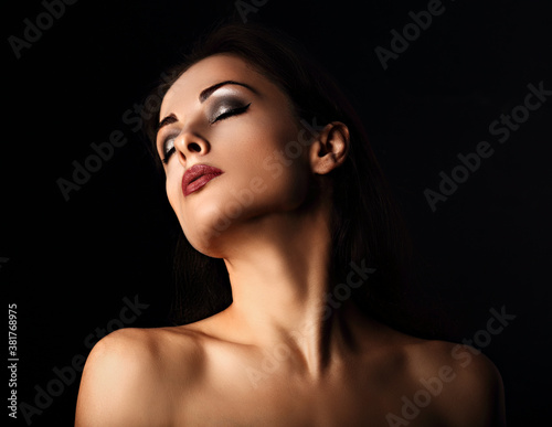 Beautiful mysterious smokey eyes makeup woman in darkness posing with healthy tan yellow skin tone elegant strong neck on black background with empty copy space. Closeup