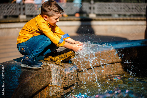 Child boy in a yellow shirt  playing with fountain strokes in summer in a park