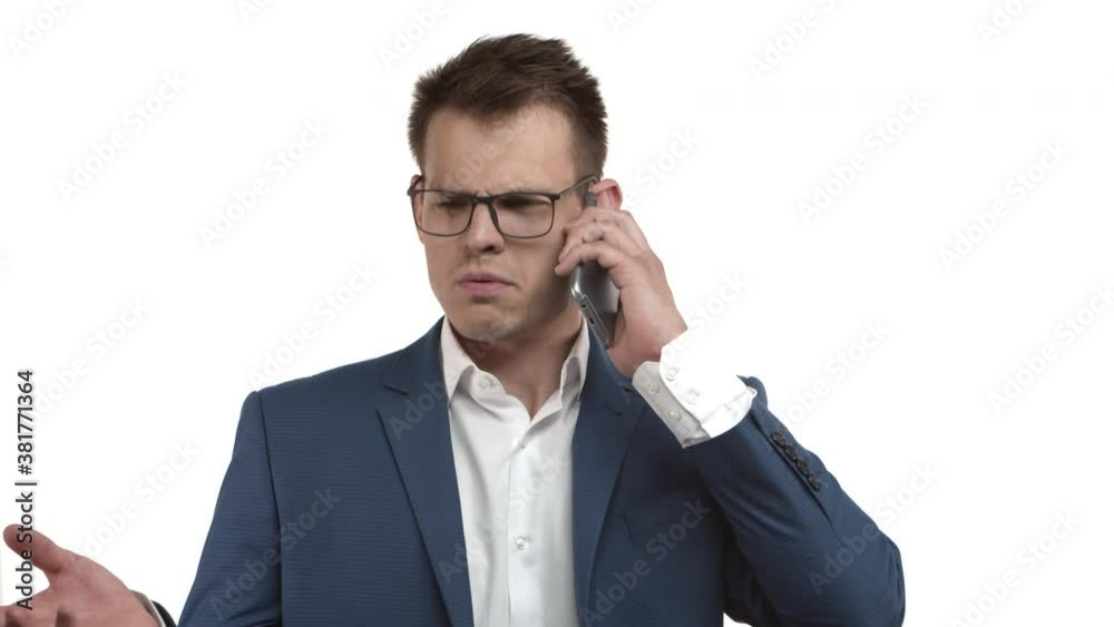 Handsome arrogant businessman in glasses and blue suit picking up phone, giving instructions to business partners, explain something during conversation, standing over white background Handsome arrogant businessman in glasses and blue suit picking up phone, giving instructions to business partners, explain something during conversation, standing over white background