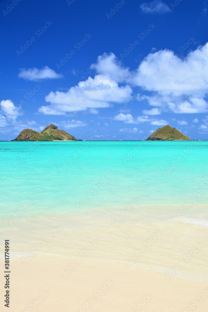 Tropical beach with turquoise waters, blue sky and view of Mokuluas at Lanikai on Oahu, Hawaii. 