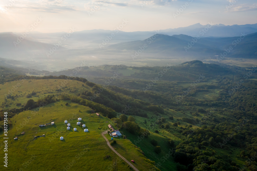 Fototapeta premium Early morning in the mountains. Morning sun and haze in the valley against the background of mountains. Mountain summer landscape. Tourist tents in the mountains
