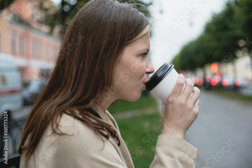 A girl drinks coffee from a cup on the street. 
