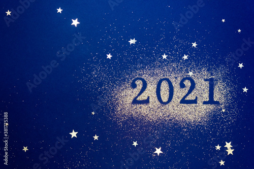 Numbers 2021 on blue background are decorated with sparkles and star confetti. New Years celebration concept. Copy space