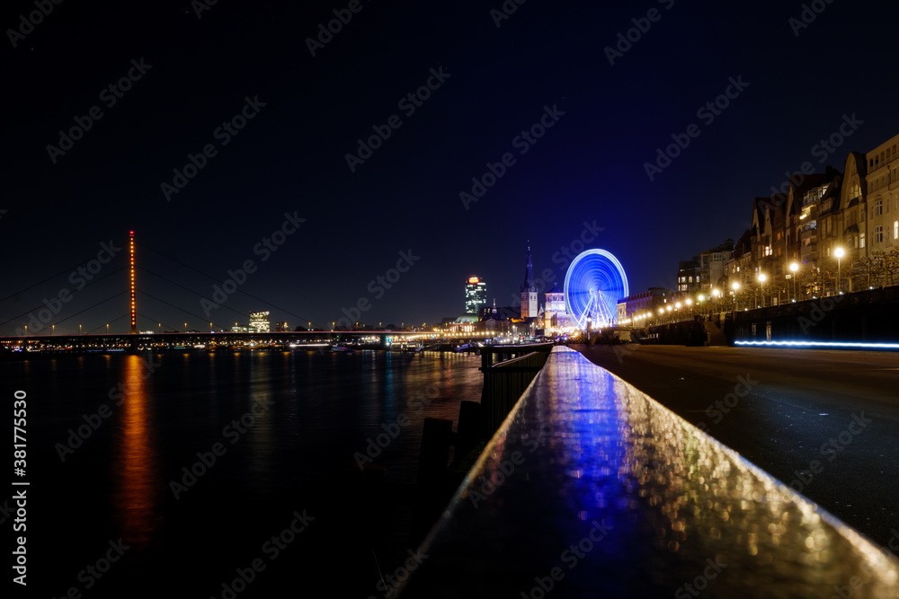 Night scenery over fence on promenade along riverside of Rhine river and background of Ferris wheel at Christmas market and cityscape in Düsseldorf, Germany.