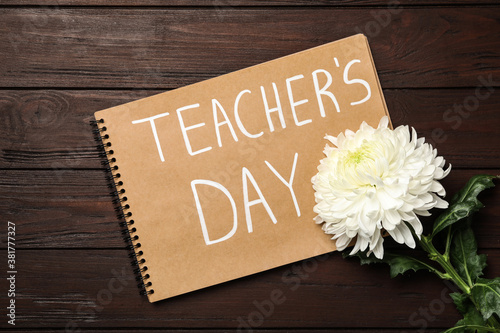 Notebook with words TEACHER'S DAY and flower on wooden table, flat lay