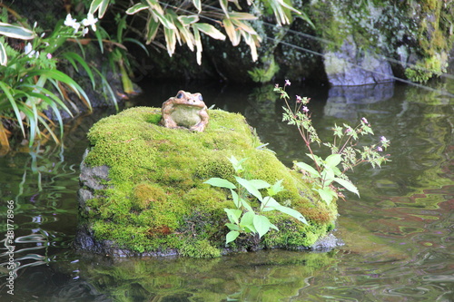 カエルの置物が乗せられ苔が生えた、池から島のように突出した岩 photo