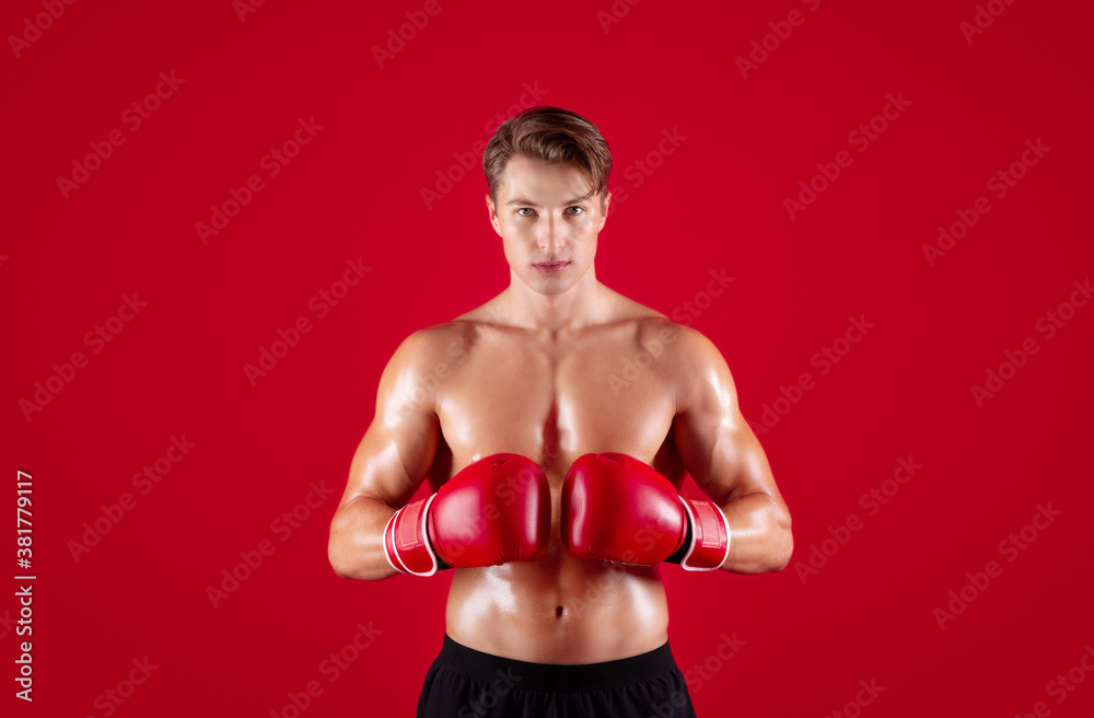 Professional boxing concept. Muscular athletic boxer putting his gloves together on red studio background Professional boxing concept. Muscular athletic boxer putting his gloves together on red studio background