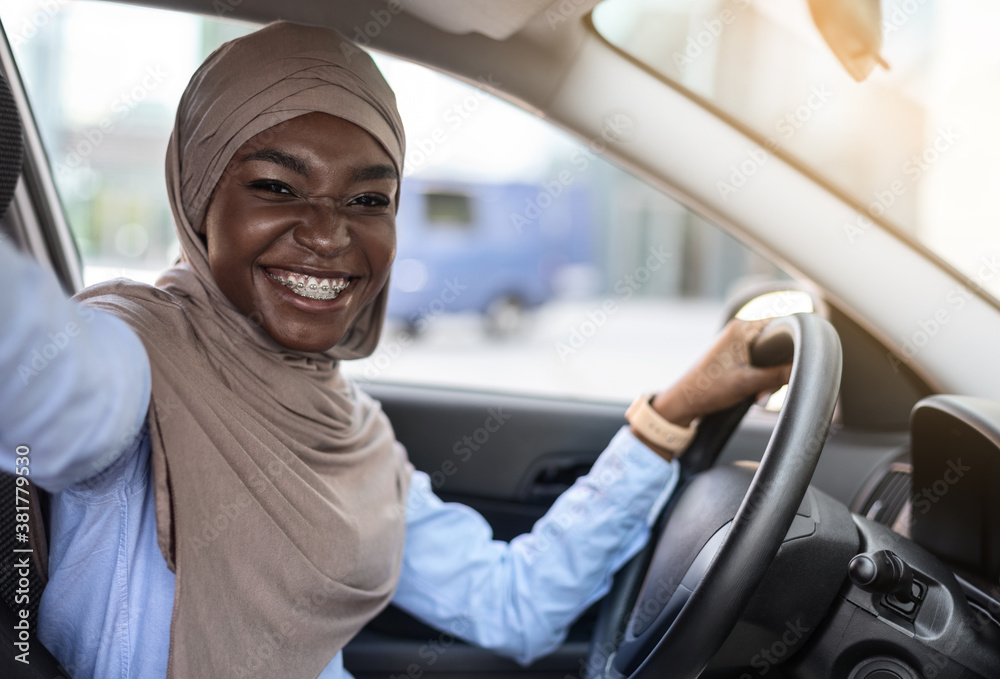 Car Selfie. Cheerful black muslim woman taking self-portrait in her new auto Car Selfie. Cheerful black muslim woman taking self-portrait in her new auto