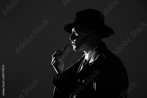 Old fashioned detective with smoking pipe on dark background  black and white effect