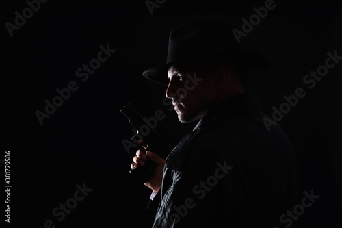 Old fashioned detective with gun on dark background. Space for text