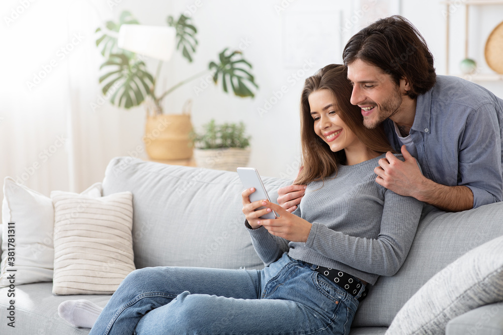 Positive young couple using mobile phone at home